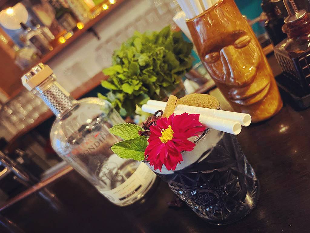 Cocktail fleuri garni d'une dahlia rose, menthe fraîche et paille blanche dans un bar